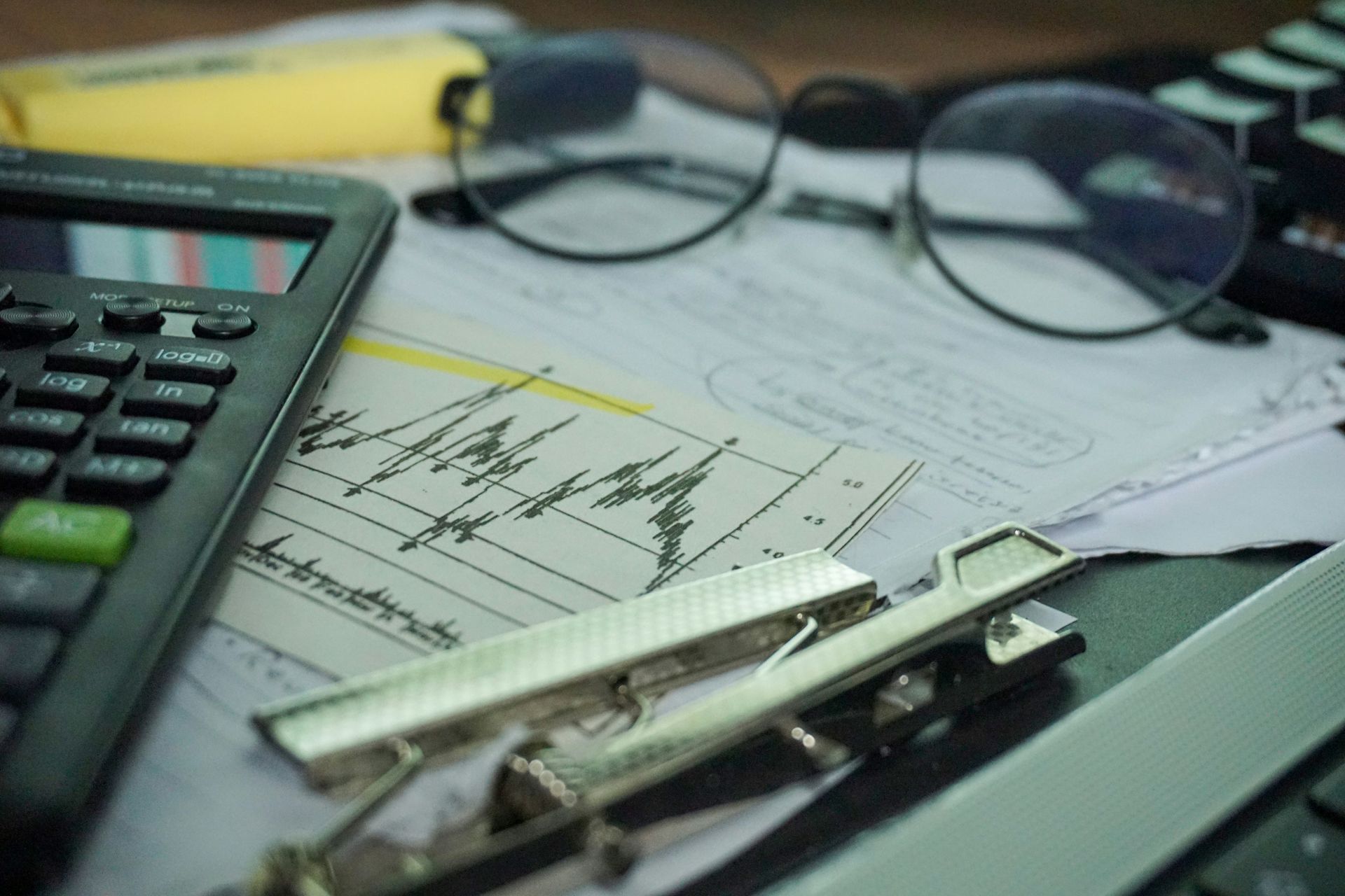 A desk with a calculator, papers, eyeglasses, and office supplies.